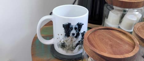 Una taza con diseño de perro, frascos de madera y una cafetera sobre una mesa.