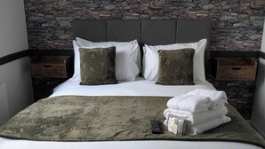 A neatly made bed with a grey headboard, two white pillows, two green pillows, a grey throw blanket, and a stack of white towels. - Gilpin Bridge Inn (Kendal)
