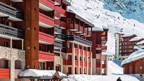 Een hotel met meerdere verdiepingen, balkons en skipistes op de achtergrond.