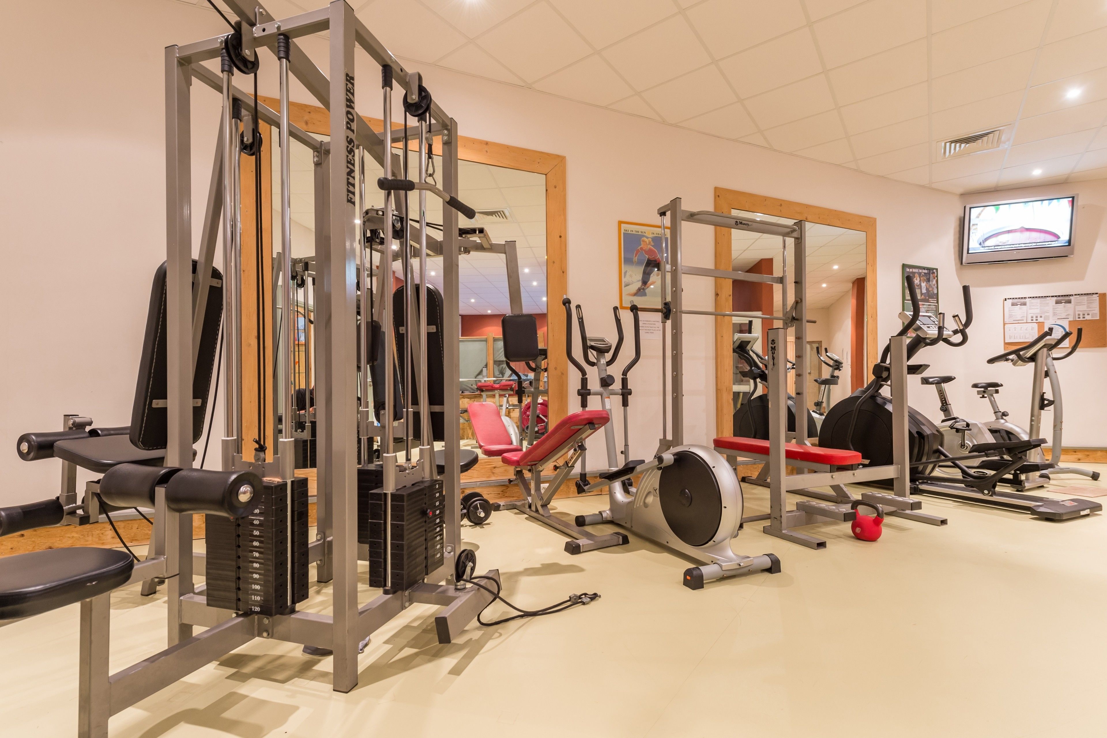 Un gimnasio con varios equipos de ejercicio, incluyendo una máquina de poleas, una banca y una elíptica.