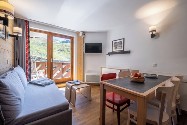 Una habitación moderna con sofá, mesa de comedor, sillas, televisor y vista a un paisaje montañoso a través de un amplio ventanal corredero.