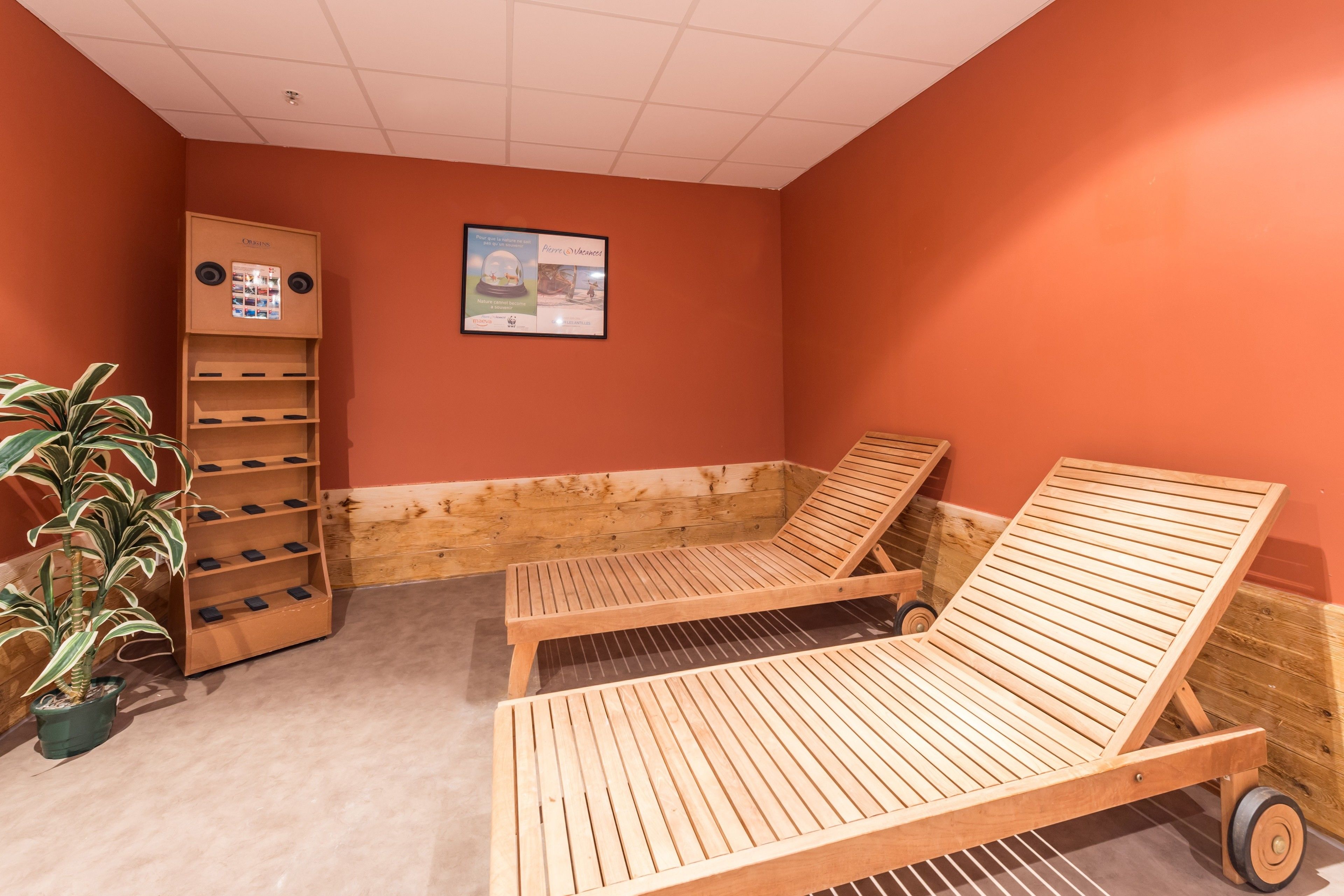 A room with two wooden lounge chairs, a wooden shelf unit with phone slots, and a potted plant.