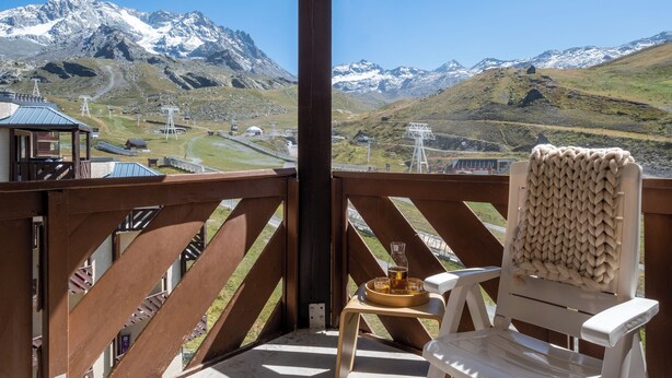 Een balkon met uitzicht op besneeuwde bergen, een houten stoel en een dienblad met een drankje.