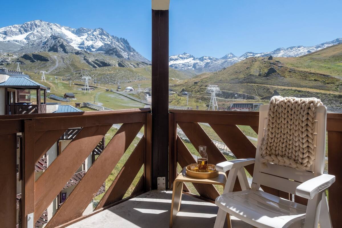A balcony with a view of snow-capped mountains, a wooden chair, and a tray with a drink.