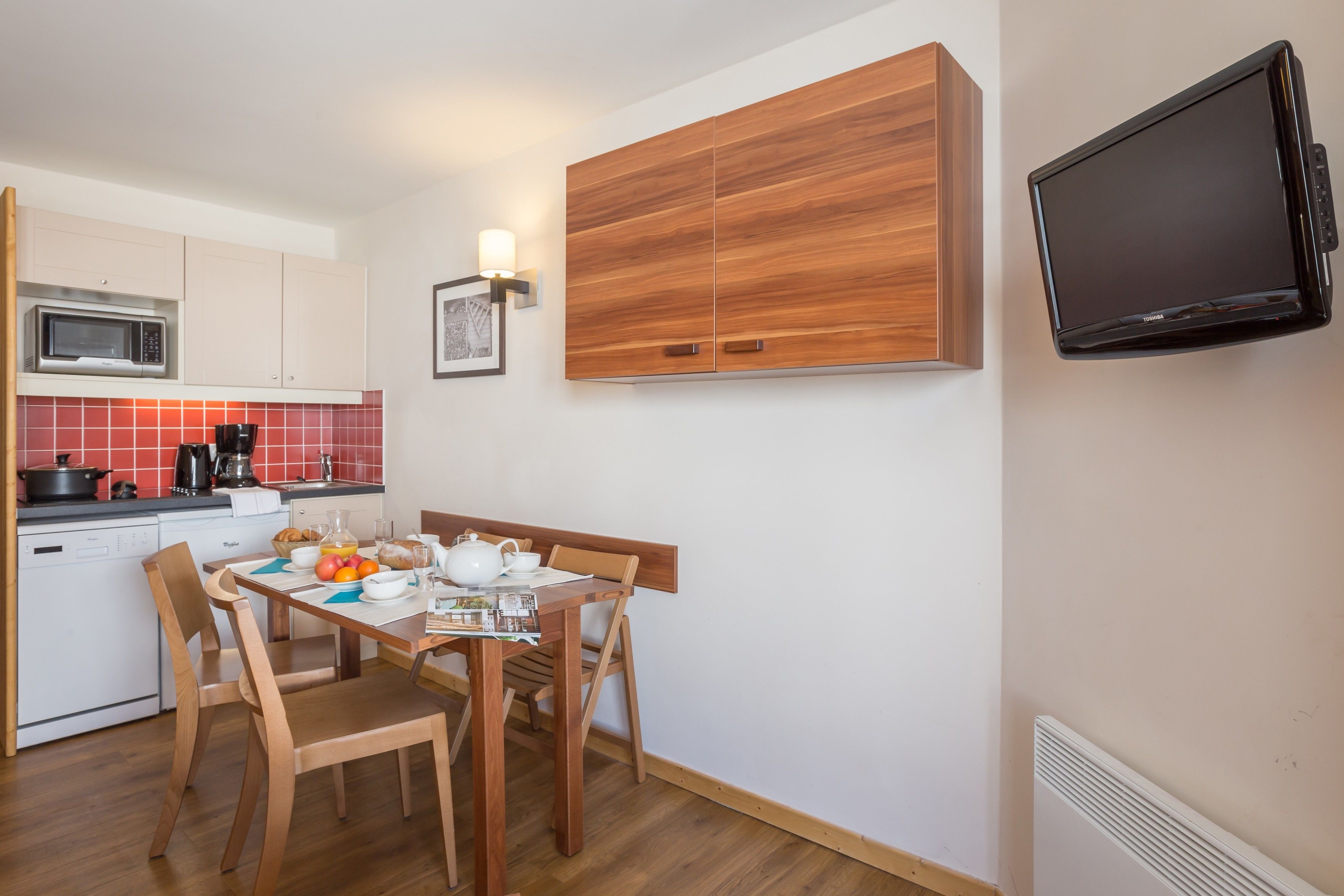 A compact kitchen with a microwave, stove, and sink. A dining table with chairs and a television mounted on the wall.
