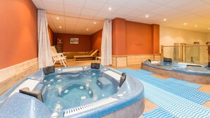 Een wellnessruimte met twee whirlpools, een massagetafel en een douchecabine met glazen wanden.