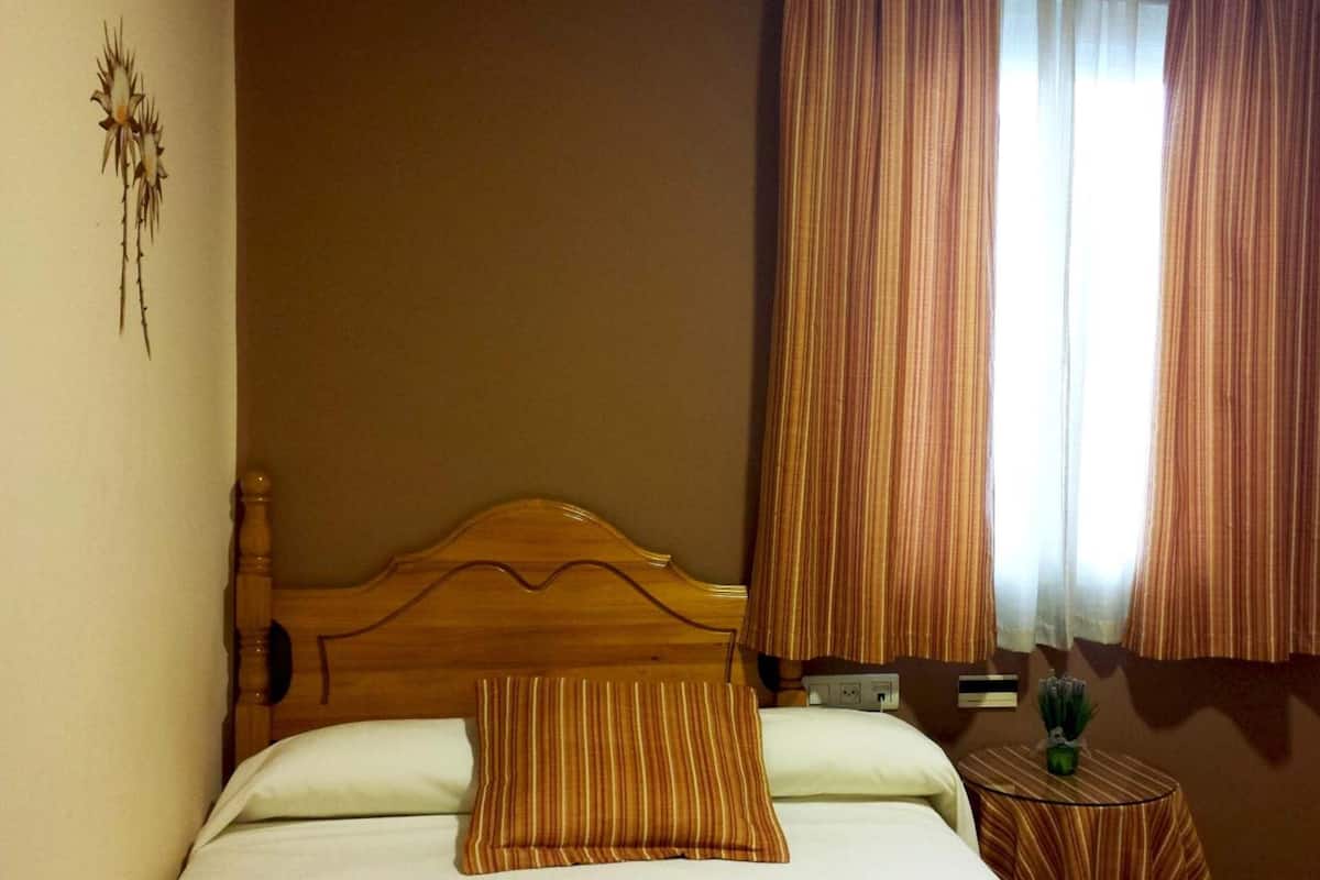 A bedroom with a wooden bed, striped curtains, and a small bedside table with a plant.
