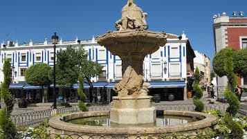 A fountain with a statue in the center, surrounded by a circular fence and flower beds.