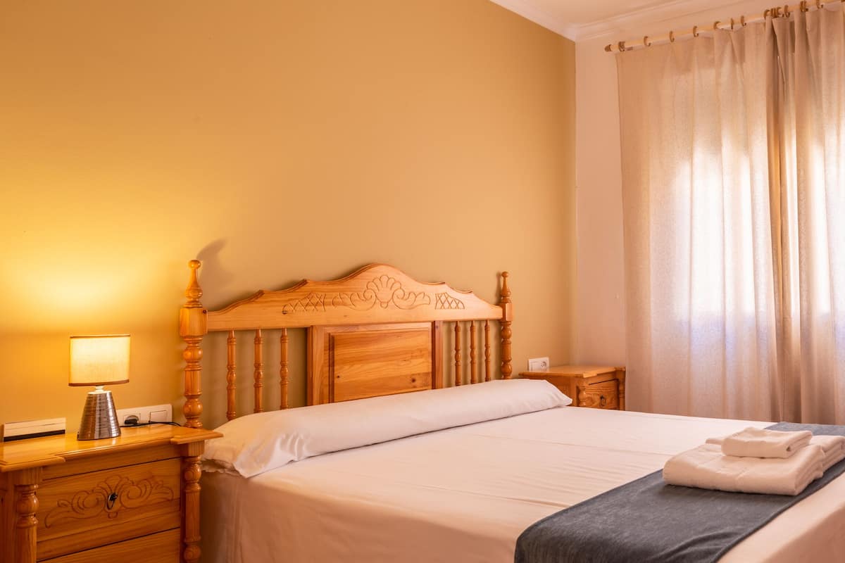 A neatly made bed with a wooden headboard, a bedside table with a lamp, and a small wooden nightstand.