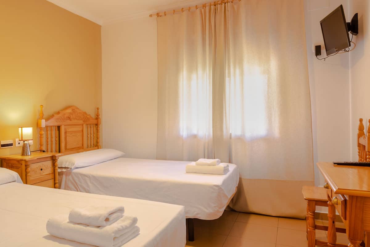 A hotel room with two wooden beds, a desk, and a television on the wall.