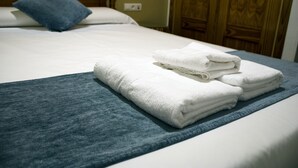 A neatly made bed with white linens and a folded blue towel on a blue bedspread. - Hostal Valdepeñas by Bossh Hotels (Valdepenas)
