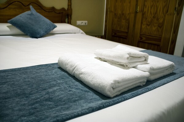 A neatly made bed with white linens and a folded blue towel on a blue bedspread.