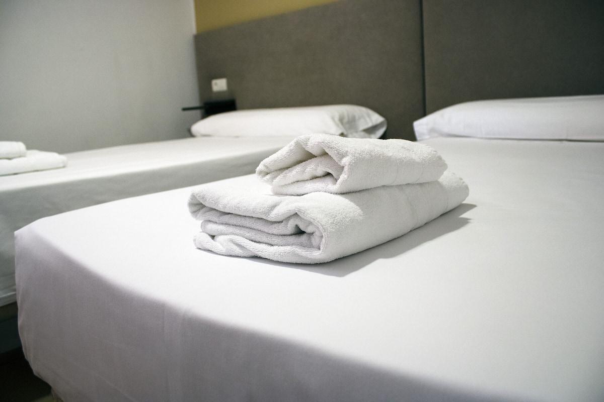 A hotel room with two beds, each with white linens and pillows.
