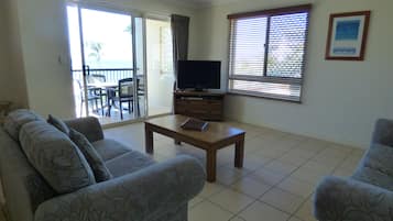 A living room with a sofa, a coffee table, a TV, and a balcony with a table and chairs.