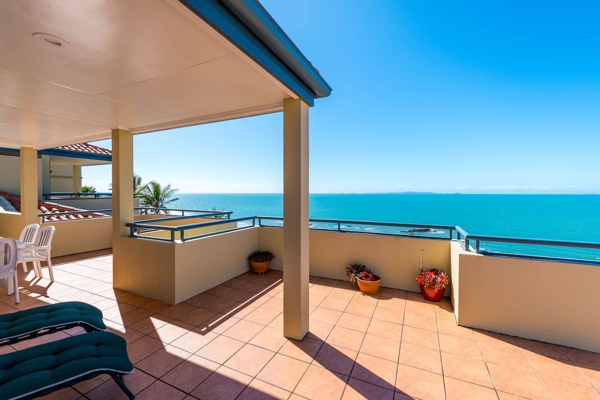 Un espacio al aire libre cubierto con vista al mar, que cuenta con un área de estar con sillas y una mesa, y plantas en macetas.