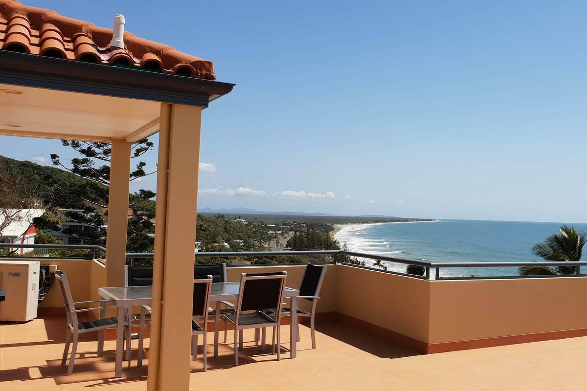 Un balcón con vista al océano, una mesa con sillas y una zona cubierta con calefacción.