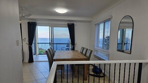 A dining area with a table and chairs, a balcony with a view, and a ceiling fan. - Villa Mar Colina (Yeppoon)
