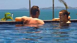 A couple in a swimming pool with a view of the ocean and palm trees. - Villa Mar Colina (Yeppoon)