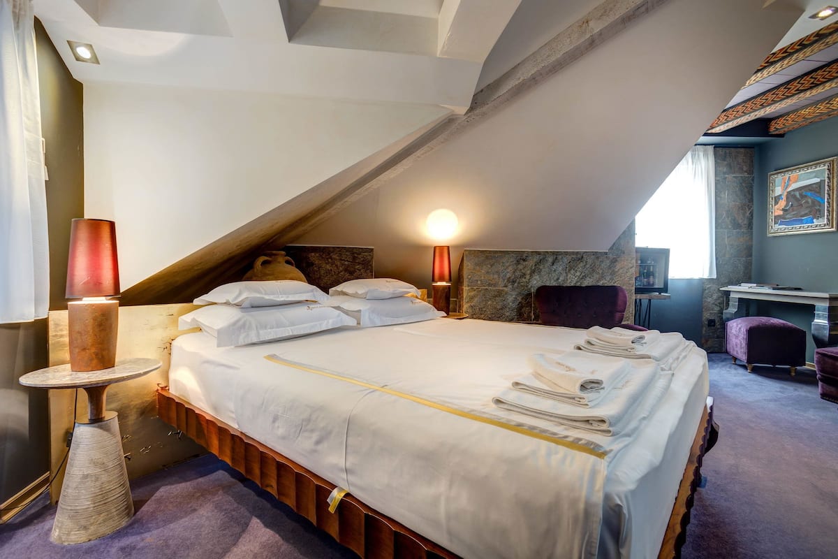 A bedroom with a large bed, a bedside table, a lamp, and a chair.