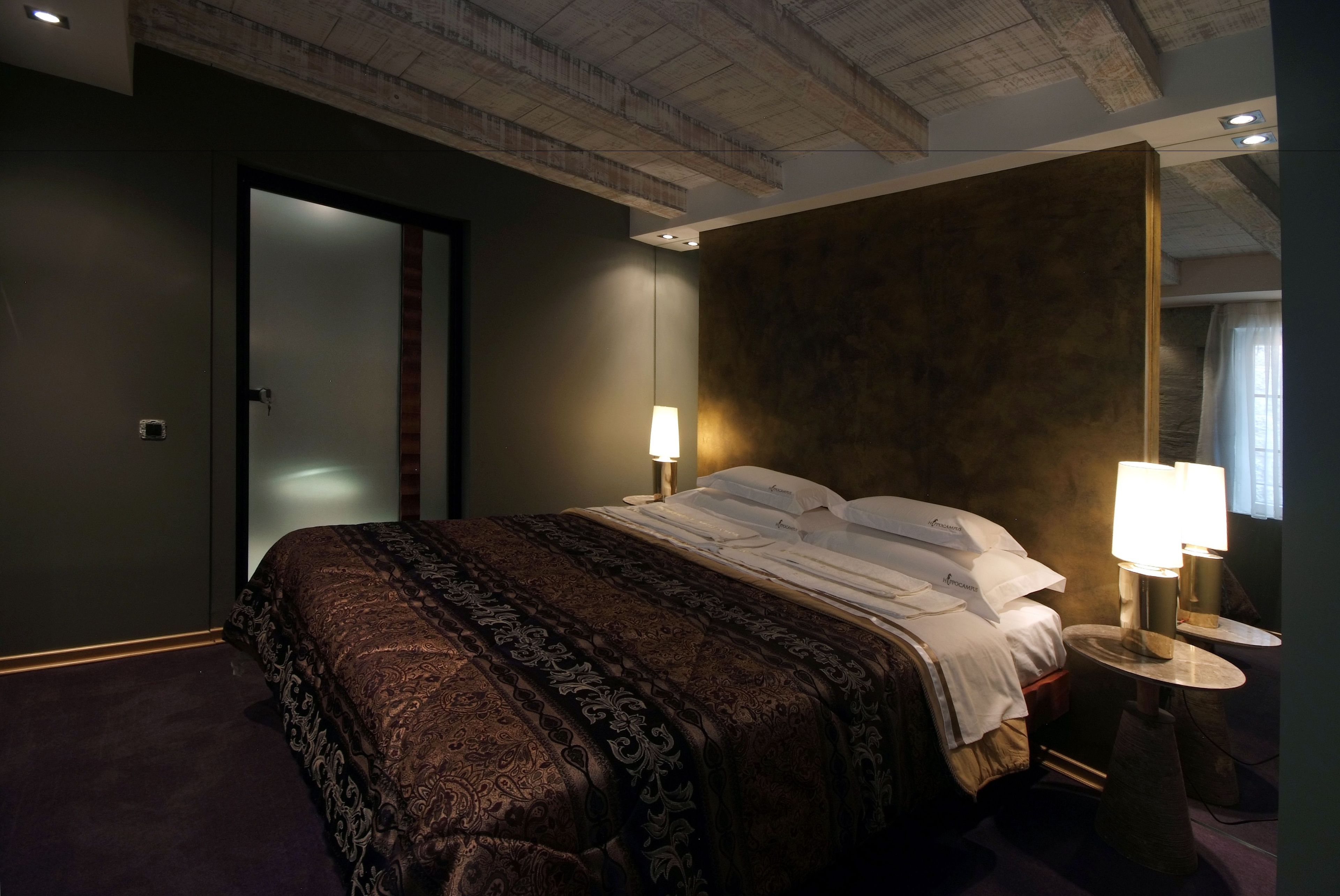 A hotel room with a large bed, two bedside lamps, a dark-colored headboard, and a visible door.