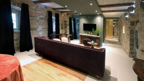 Una sala de estar moderna con pared de piedra, un sofá morado, piso de madera y un televisor de pantalla plana montado en la pared.