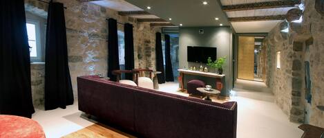 A modern living room with a stone wall, a purple sofa, a wooden floor, and a flat-screen TV mounted on the wall.