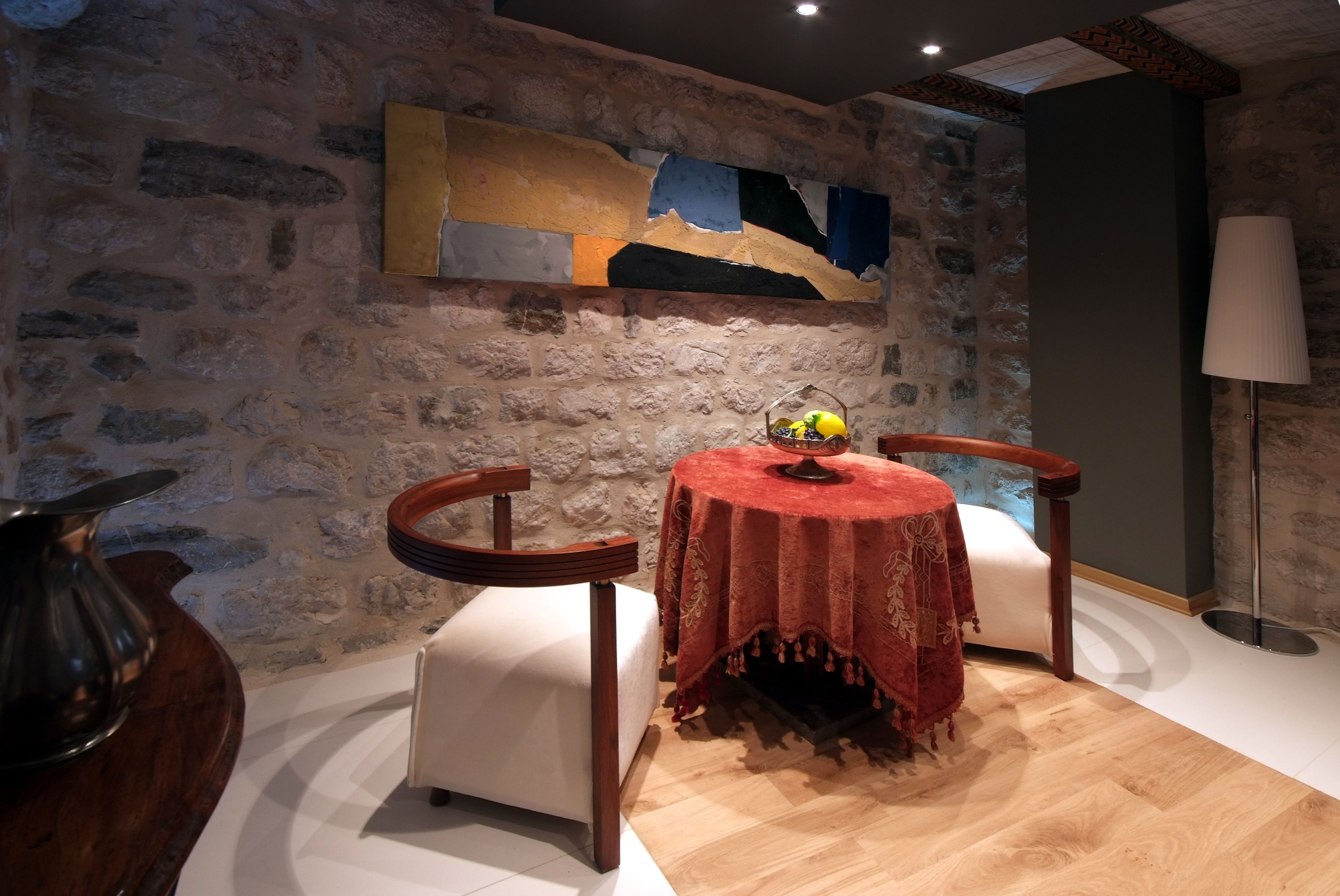 A cozy room with a stone wall, a round table with a red tablecloth, two chairs, and a lamp.