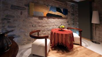A cozy room with a stone wall, a round table with a red tablecloth, two chairs, and a lamp.