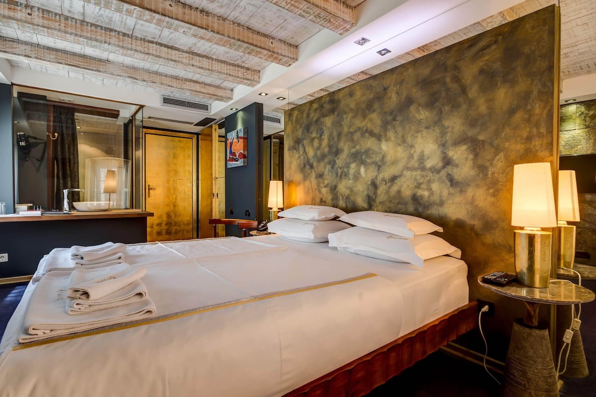 A hotel room with a large bed, a bedside table with lamps, a mirror, and a wall with a textured pattern.