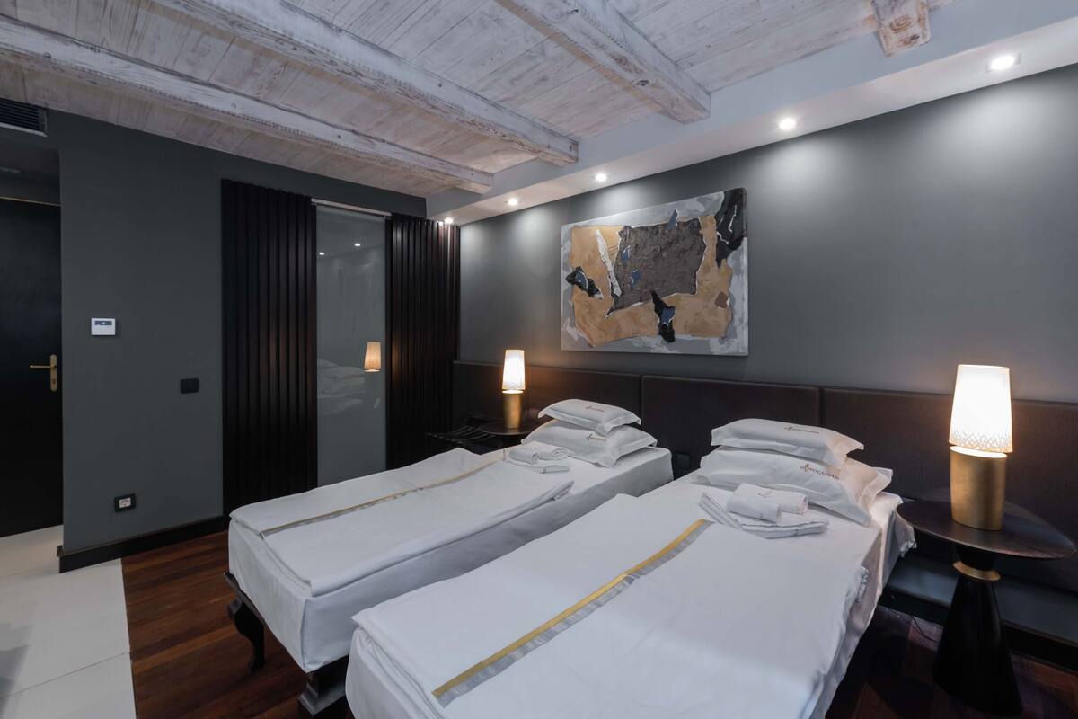 A hotel room with two beds, a large abstract painting on the wall, and two bedside lamps.