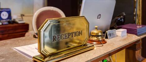 A reception desk with a glass nameplate labeled "RECEPTION," a laptop, a bell, and some documents.