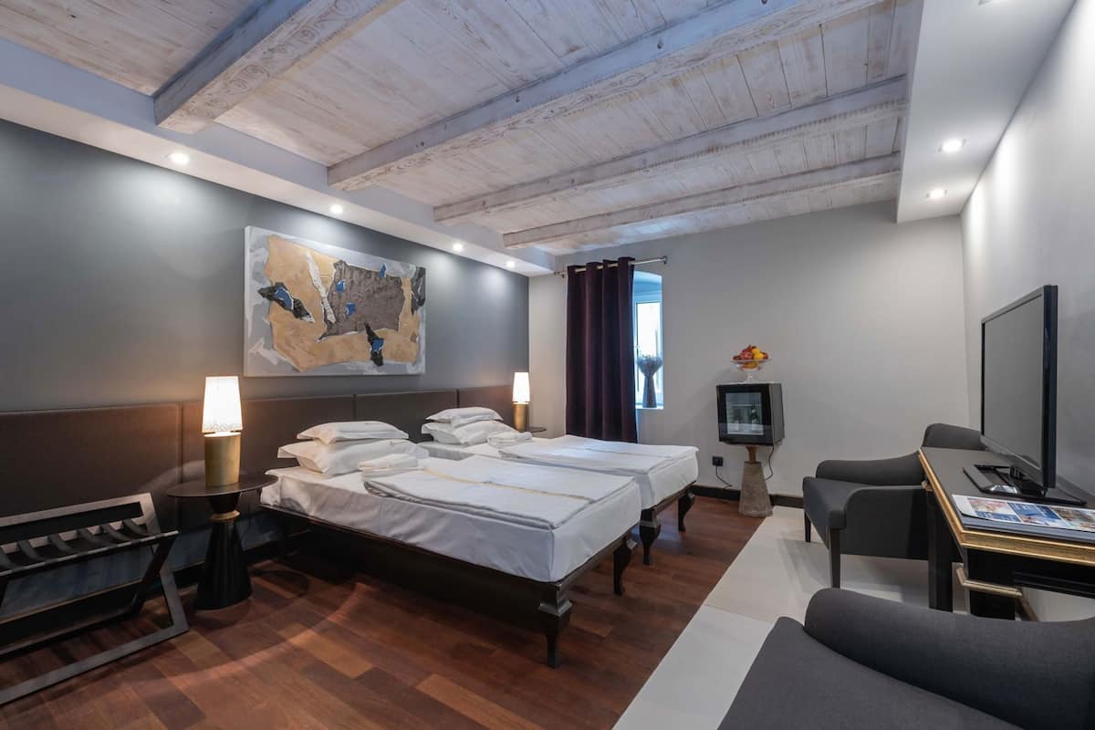 A hotel room with a bed, bedside tables, a desk with a computer, a TV, and a large abstract painting on the wall.