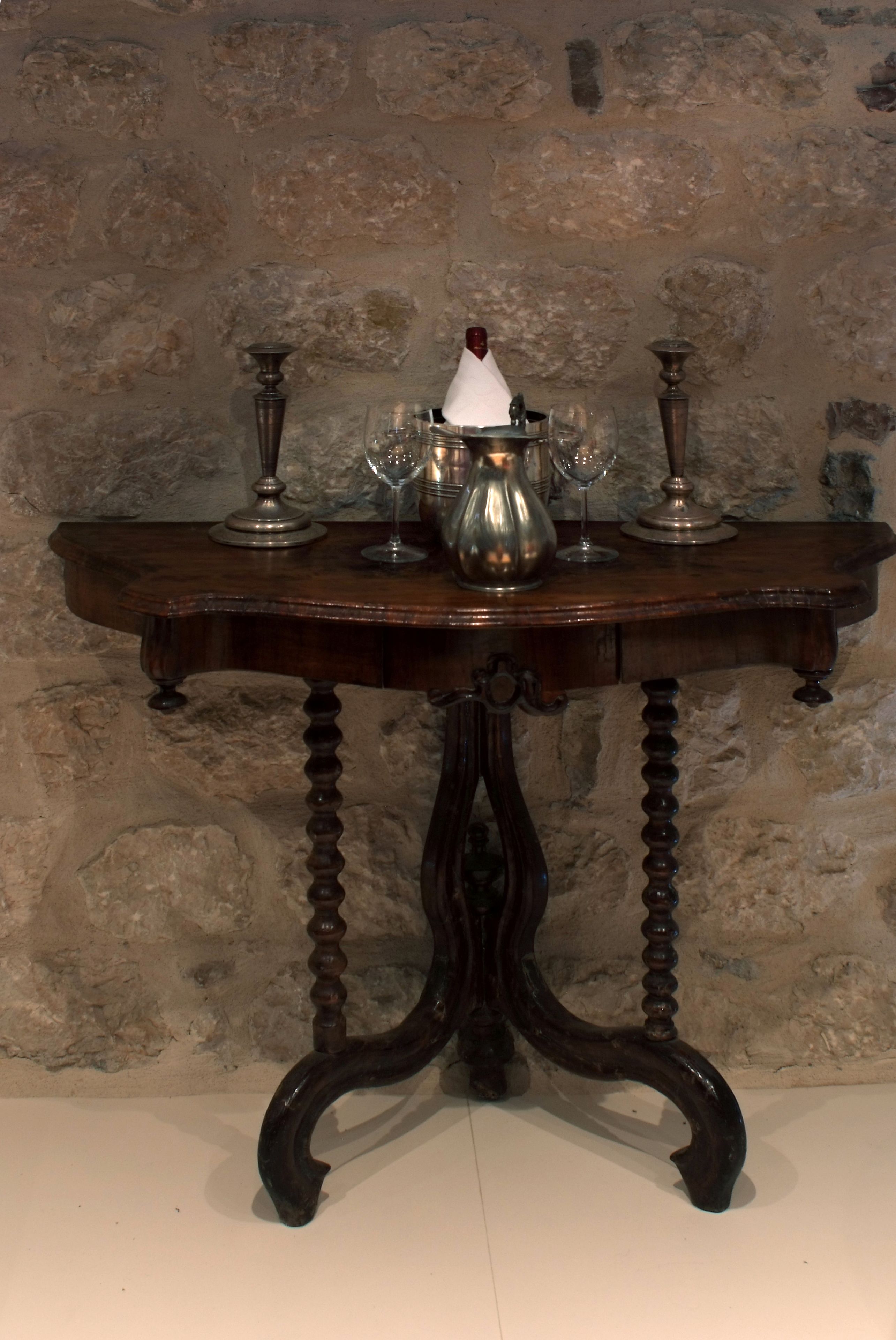 A dark wooden table with a white candle, two metal candlesticks, and a silver pitcher.