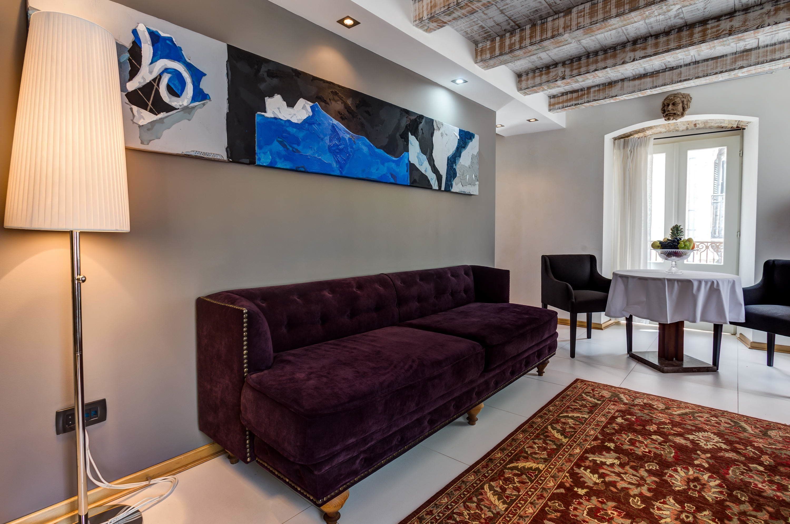 Una sala de estar moderna con un sofá de terciopelo morado, un cuadro abstracto grande, una lámpara de pie y una alfombra estampada.