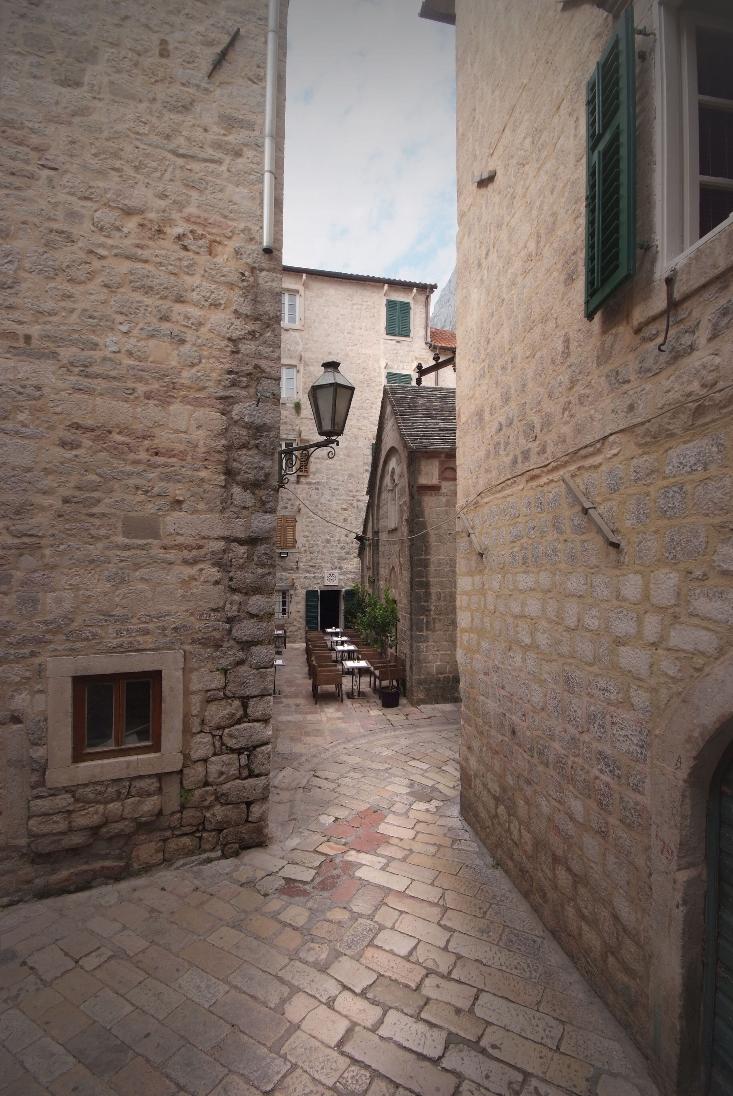 A narrow stone alleyway with a table and chairs set up, suggesting a dining area.