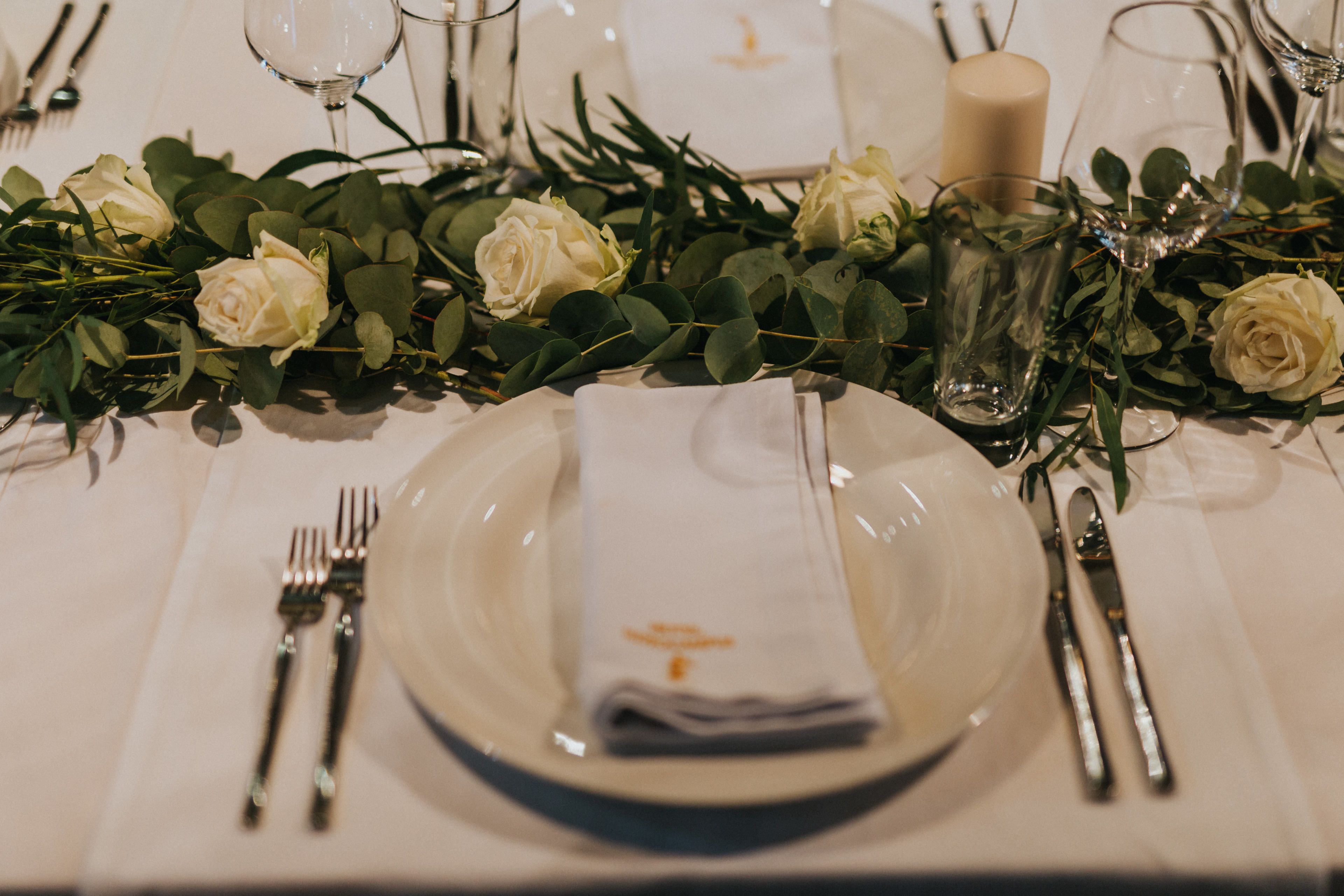 A table set with white roses, a candle, and clear glassware.