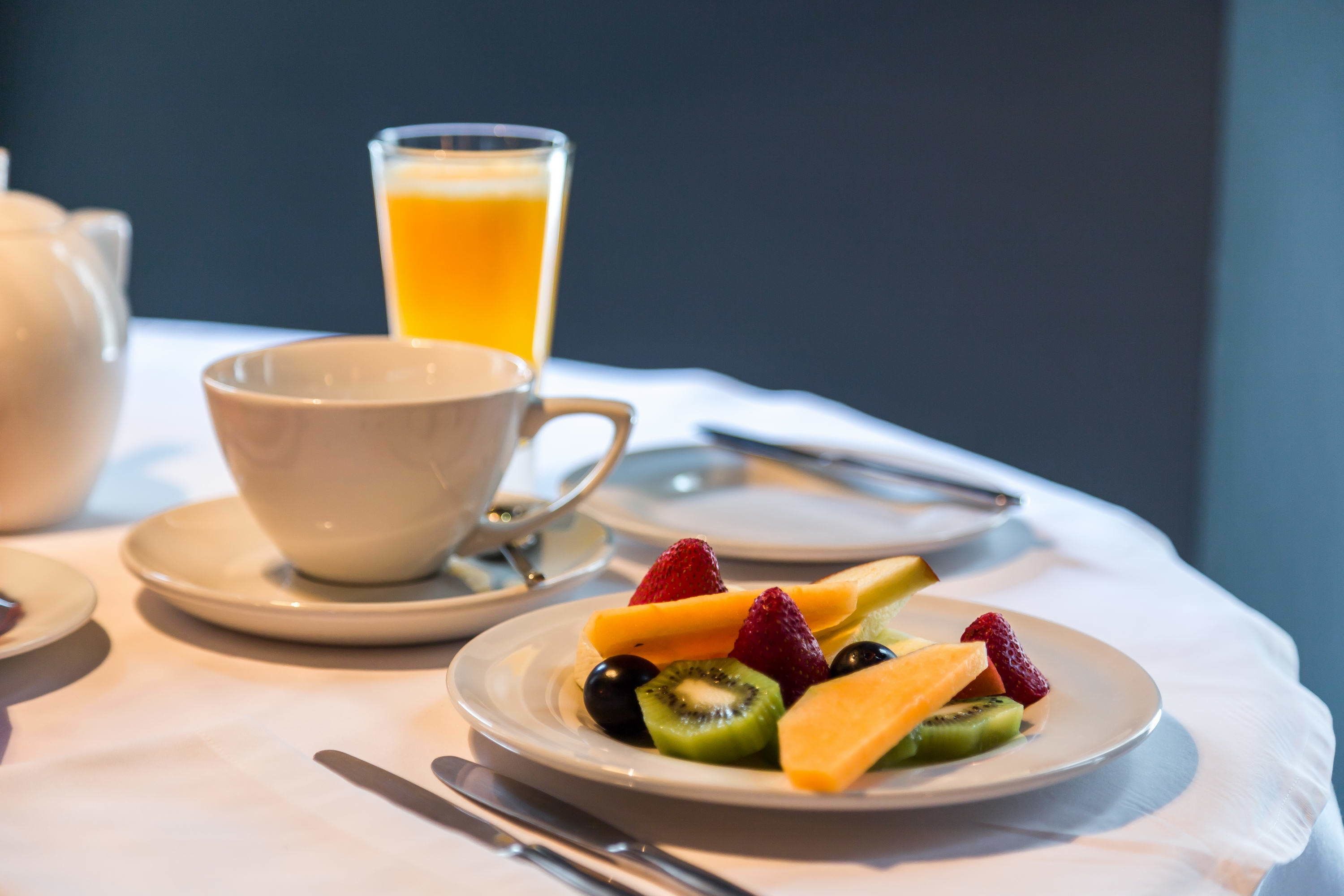 A breakfast setting with a plate of fruit, a cup of coffee, and a glass of orange juice on a table.