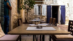 Un área de comedor al aire libre de estilo rústico, con paredes de piedra, mesas de madera y sillas con cojines.