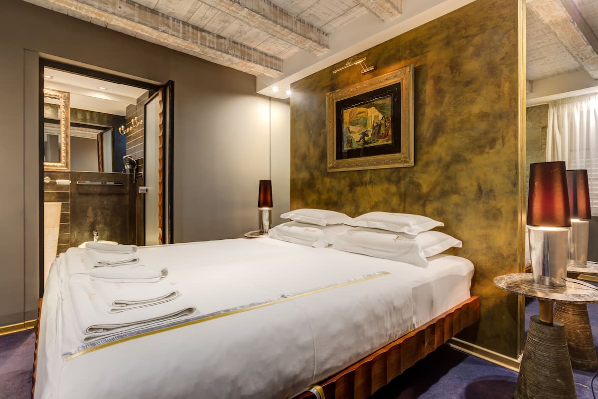 A hotel room with a bed, a mirror, a painting on the wall, and a lamp.