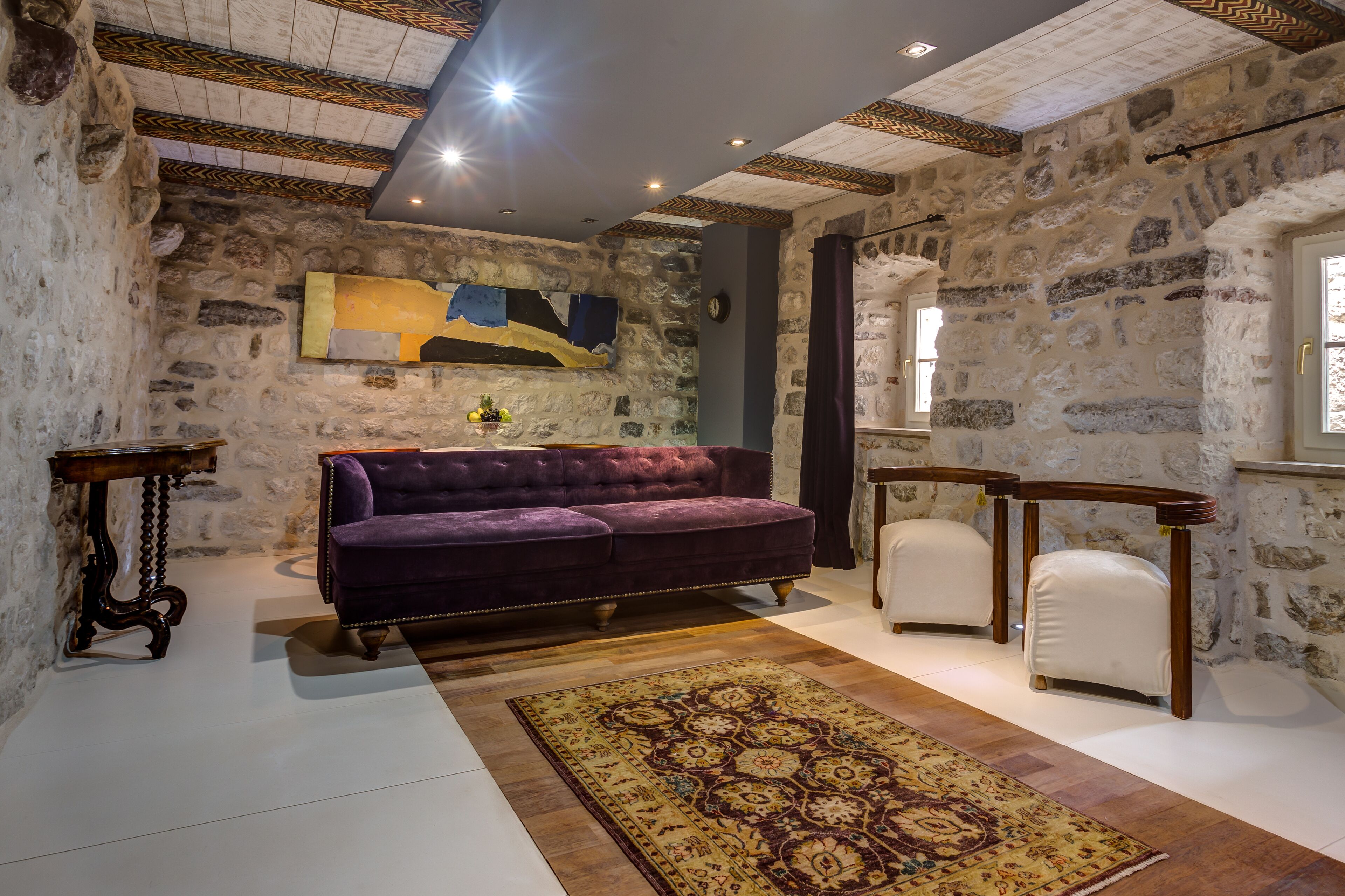 A room with stone walls, a purple sofa, a patterned rug, and wooden furniture.