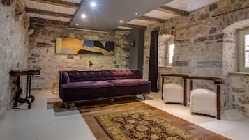 A room with stone walls, a purple sofa, a patterned rug, and wooden furniture.