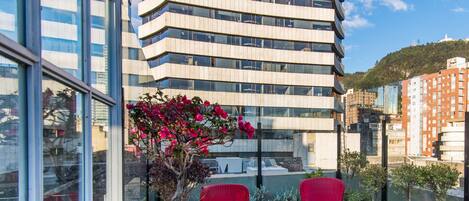 A modern building with a balcony featuring red wicker chairs and potted plants.