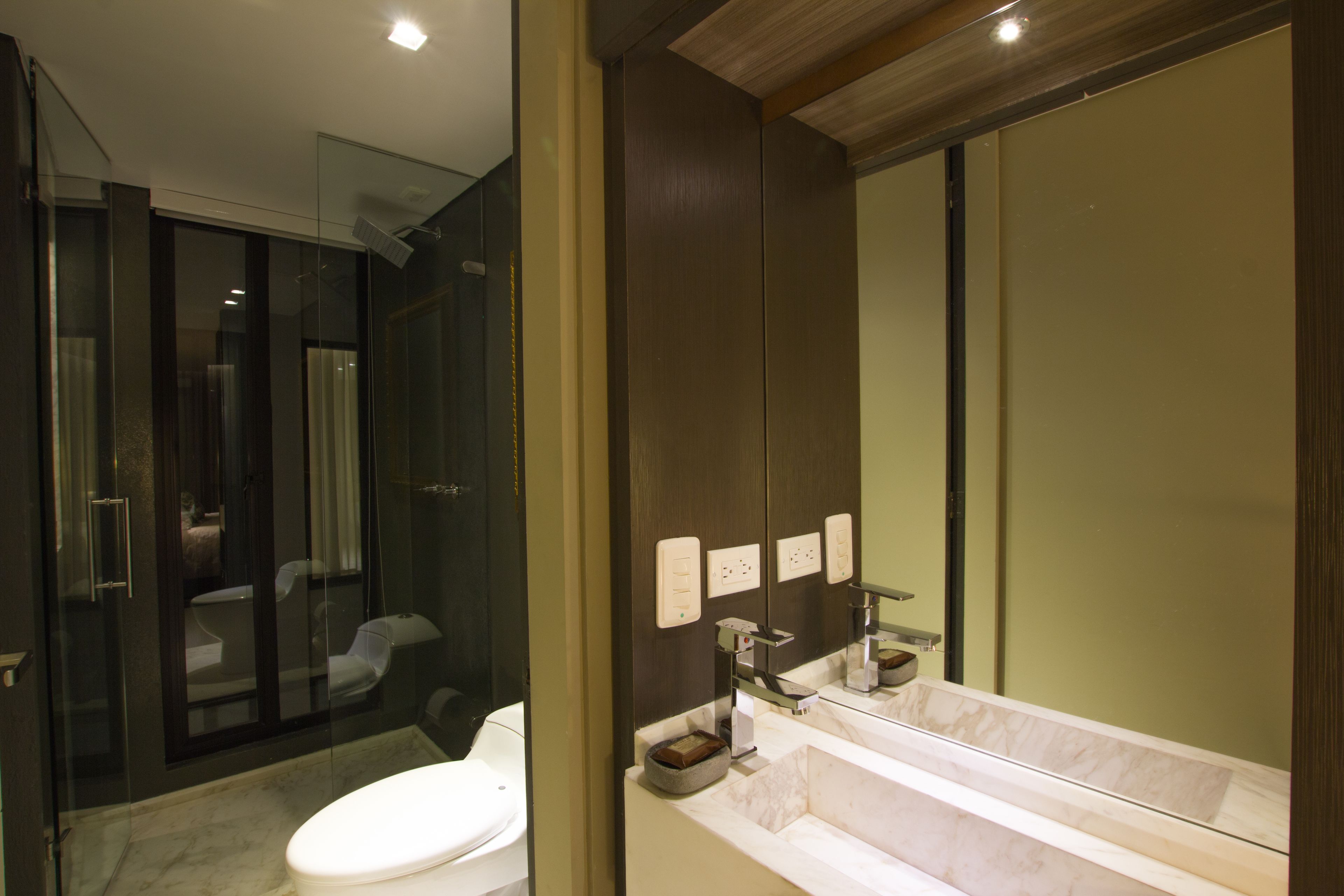 A modern bathroom with a glass shower enclosure, a white toilet, and a large mirror above a marble sink.
