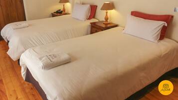 A hotel room with two beds, each with white linens and red pillows, wooden nightstands with lamps, and a wooden floor.