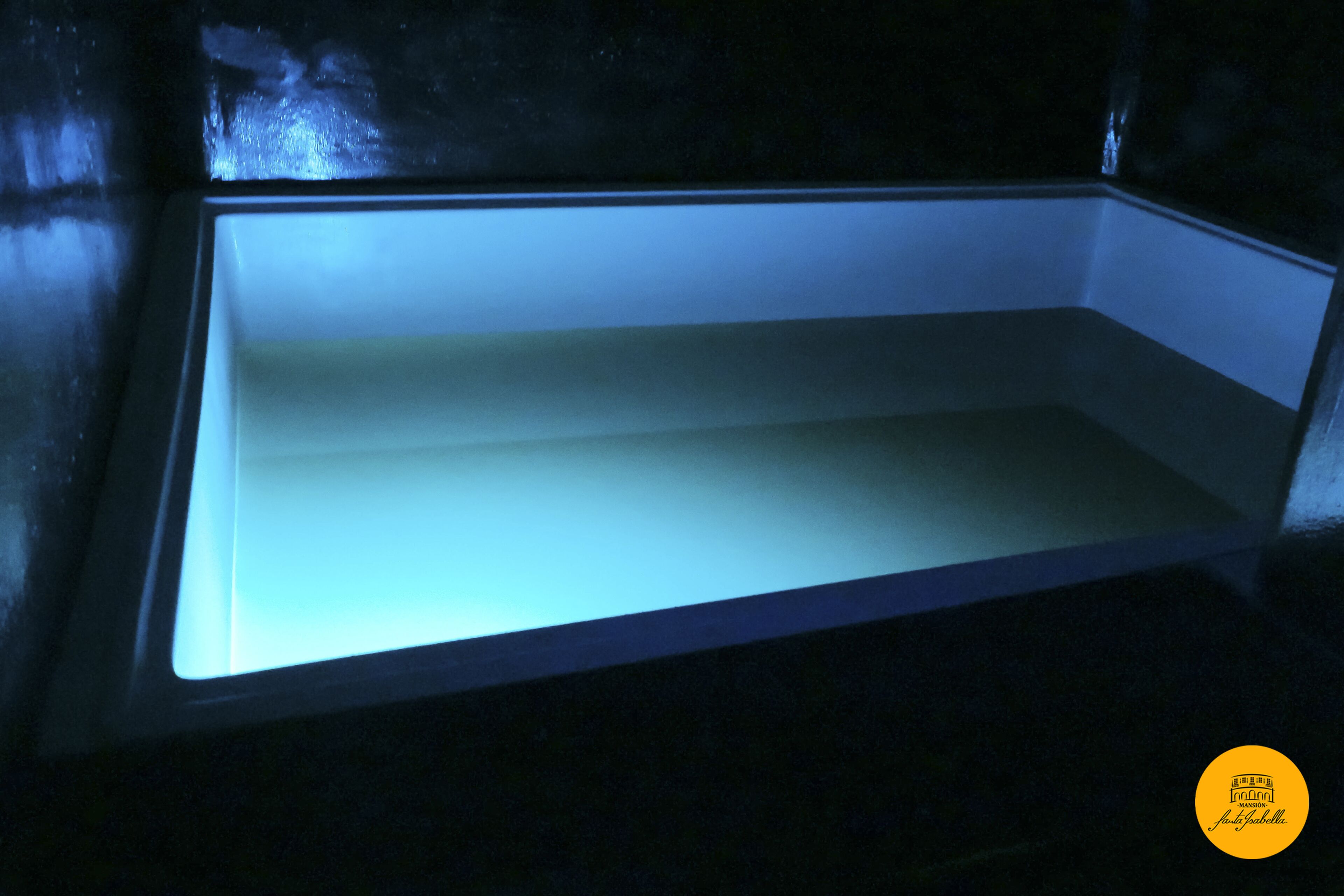 A room with a large, empty, illuminated space, possibly a pool or aquarium, and a dark, enclosed area.