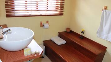 A bathroom with a large white sink, wooden bench, and a towel hanging on the wall.