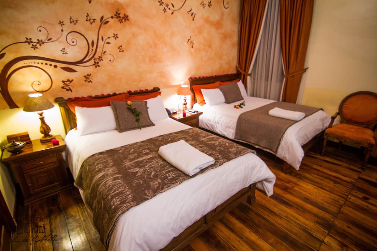Habitación de hotel con dos camas, piso de madera, una mesita de noche con lámpara y una silla.