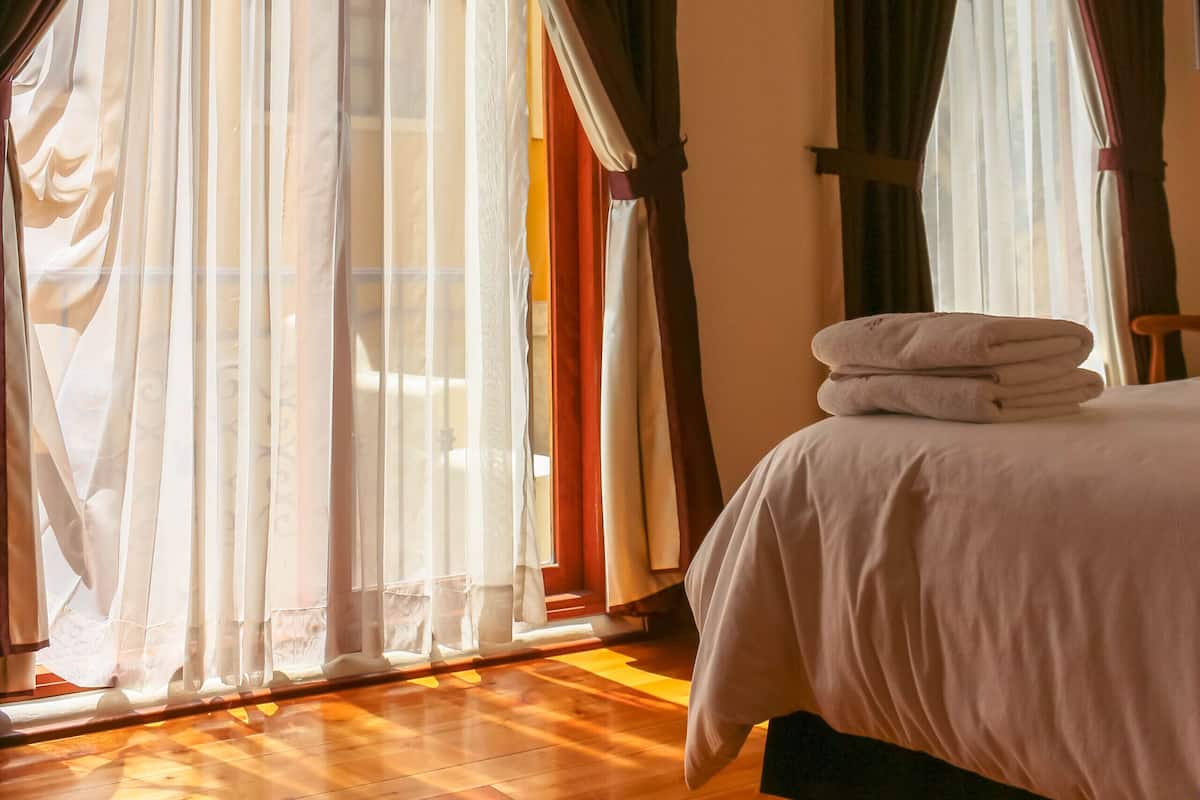 Un dormitorio con cama, piso de madera y cortinas.