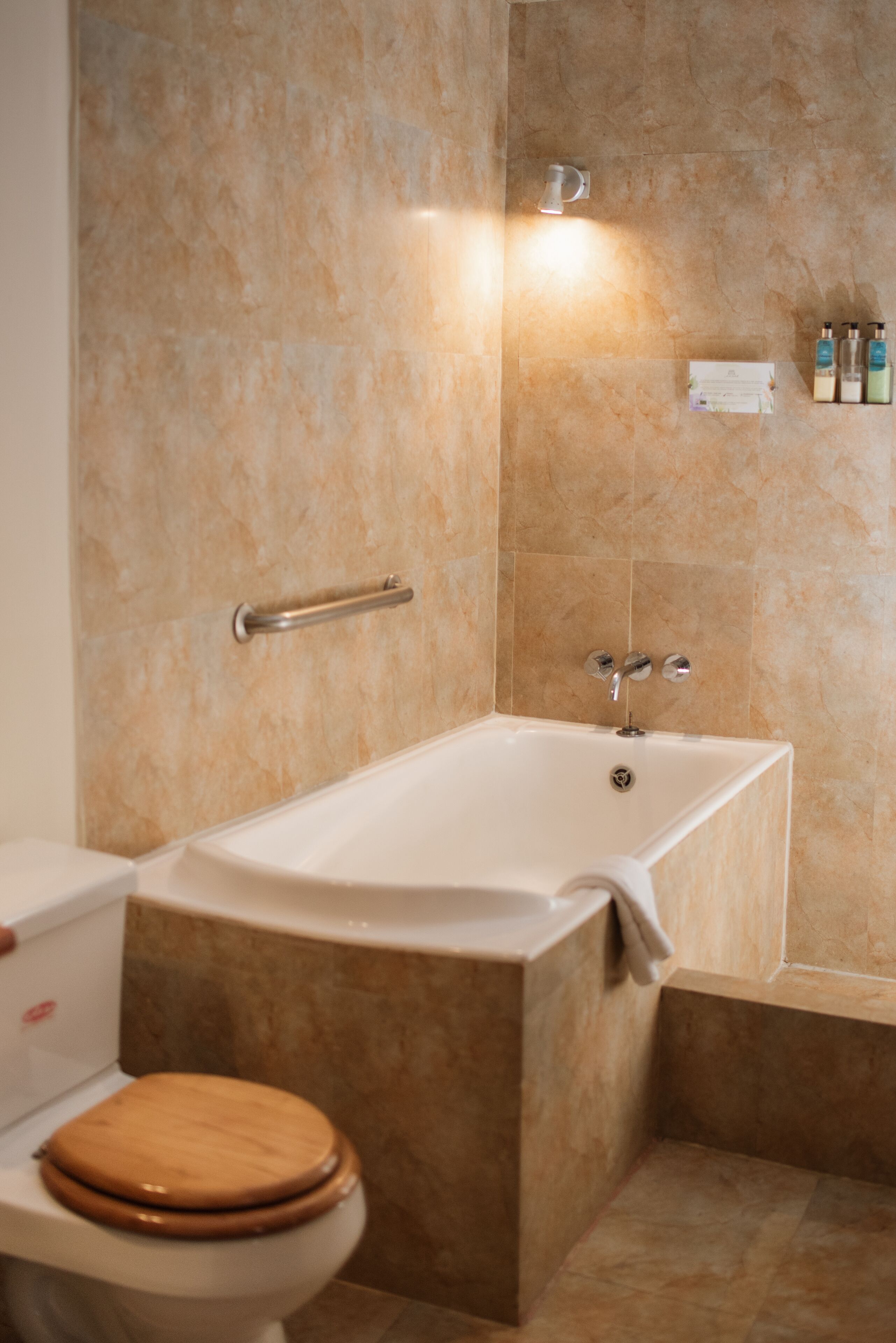 A bathroom with a bathtub, toilet, and a handrail.