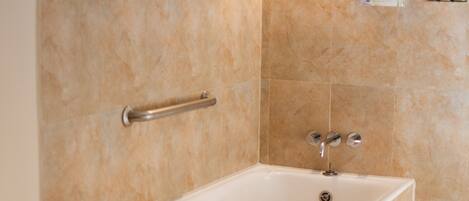 A bathroom with a bathtub, toilet, and a handrail.